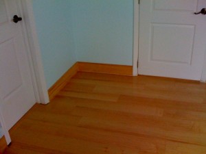 Clean wooden floor corner with white walls and a closed door.