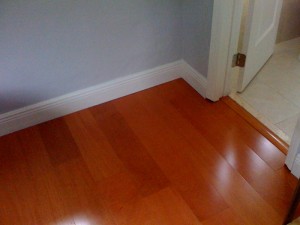 Polished wooden floor with white baseboards in a corner room.