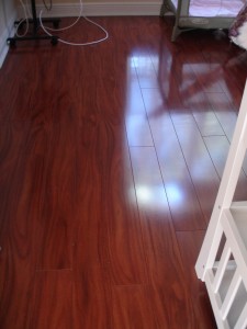 Shiny wooden floor reflecting light near a white staircase.