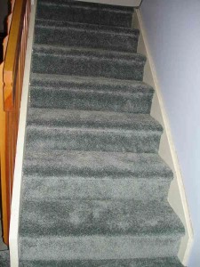 Carpeted stairs with greenish-grey carpet and wooden railing.
