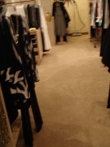 A carpeted hallway with clothes hanging on both sides in a dimly lit room.