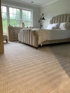 Sunlight casts striped shadows on a beige carpet in a cozy bedroom.